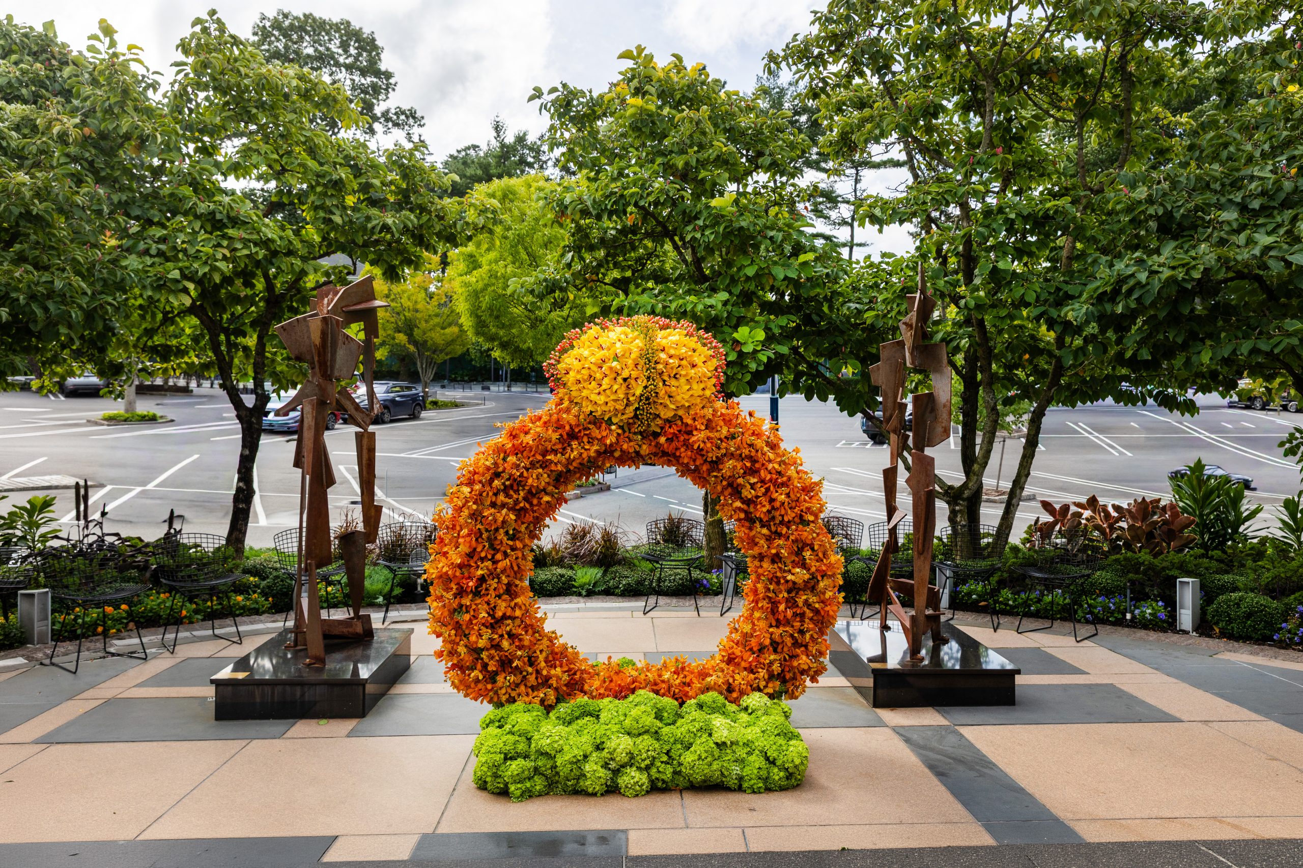Pedestals Floral Decorators’ orange and yellow floral ring installation with a green floral base at Americana Manhasset.